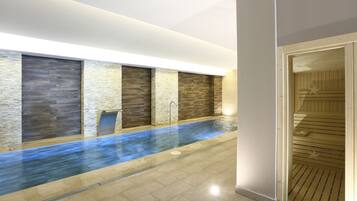 A modern indoor pool with stone walls and a wooden sauna area.