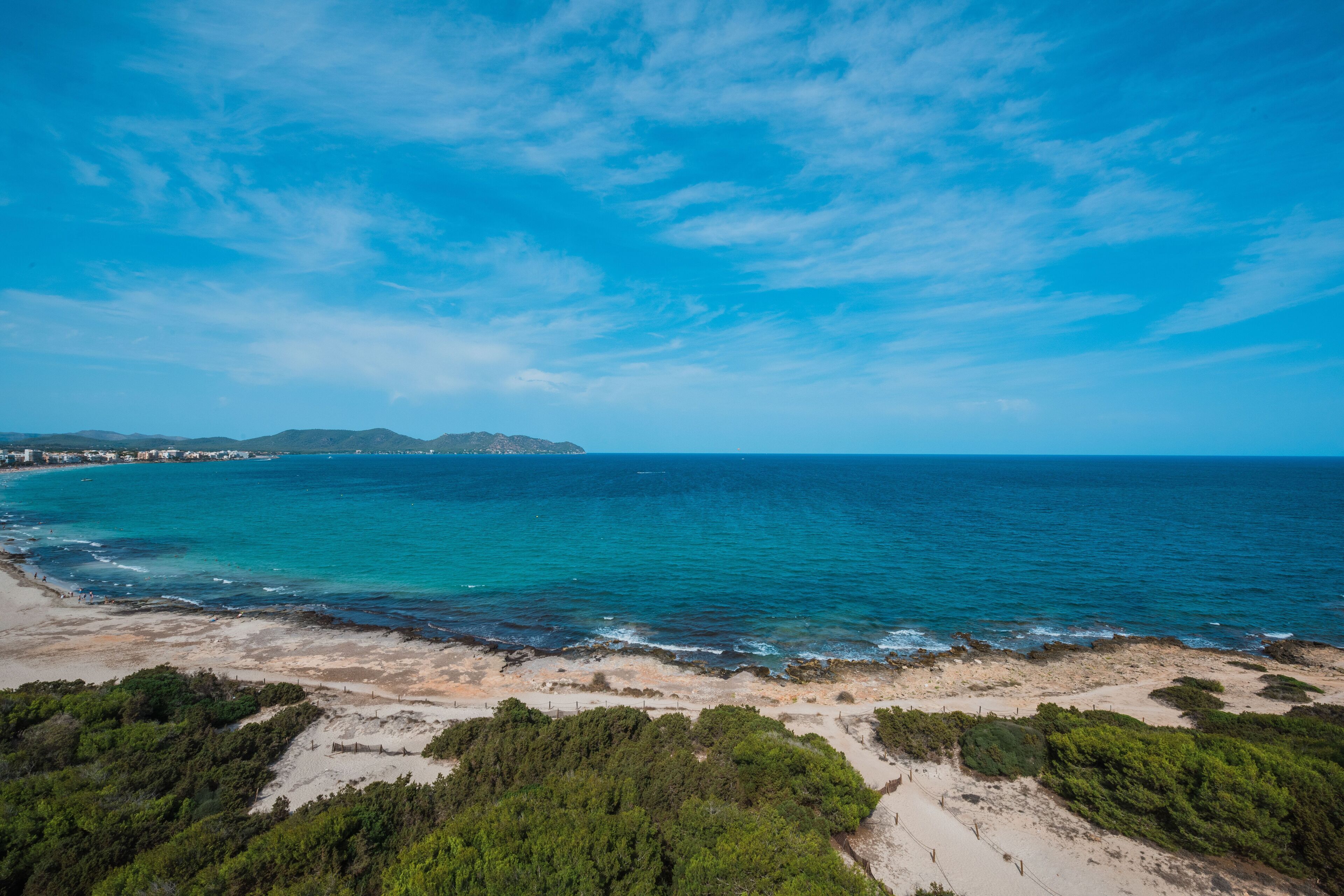 A coastal landscape with a beach, clear blue sky, and distant mountains.