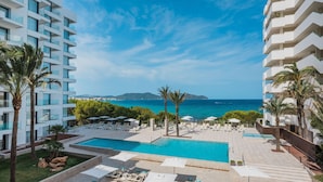 A pool area with lounge chairs and umbrellas, surrounded by palm trees and a view of the sea. - Iberostar Waves Cala Millor -Adults Only (Sant Llorenc des Cardassar)