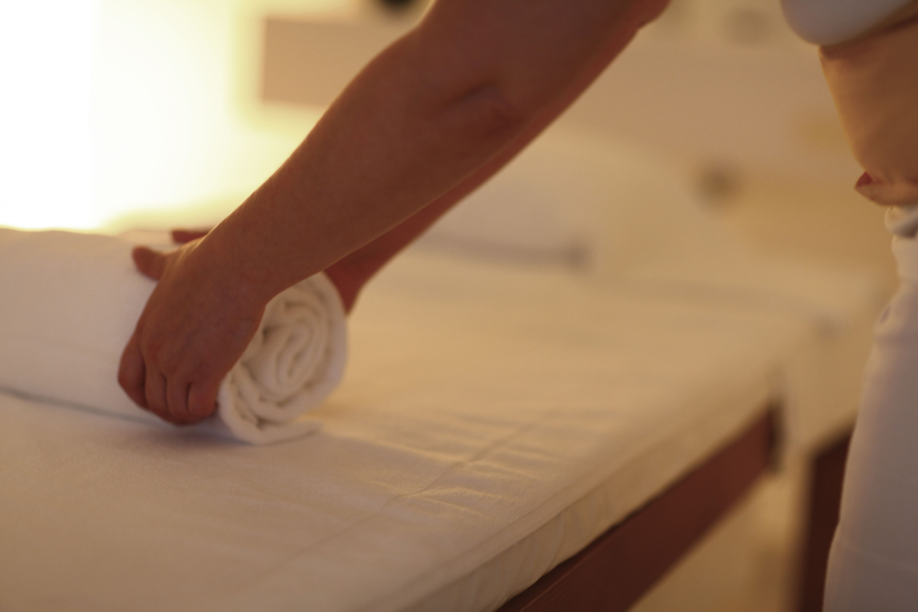 Una persona enrollando una toalla sobre la cama.