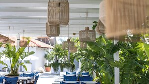 Un área de estar al aire libre con luces colgantes de mimbre, sillas con cojines azules y plantas en macetas.