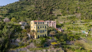 Un villaggio aggrappato alla collina con campi a terrazze, un edificio giallo con tetto rosso e un edificio rosa sullo sfondo.