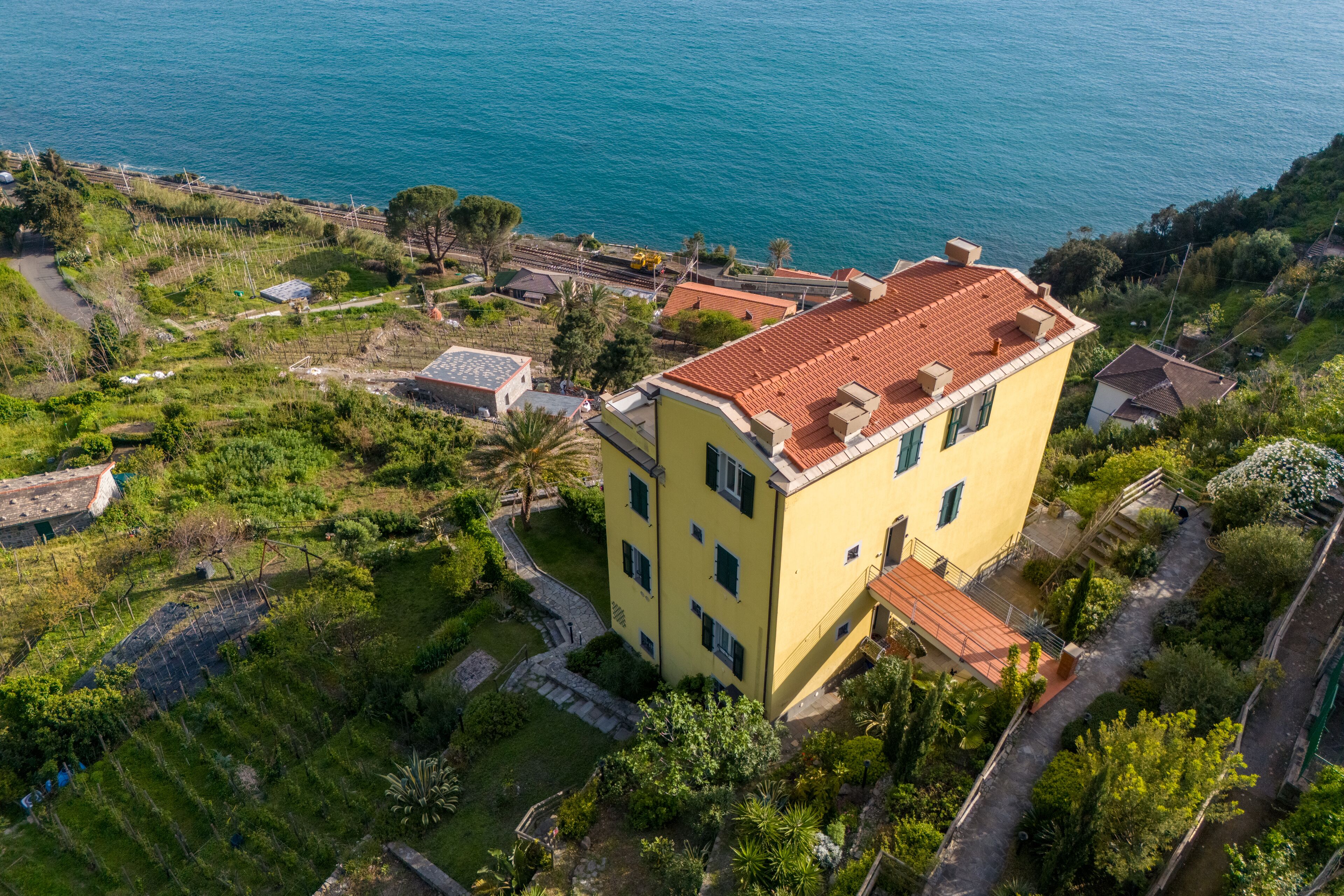 A yellow building with a red roof, surrounded by greenery and a body of water.