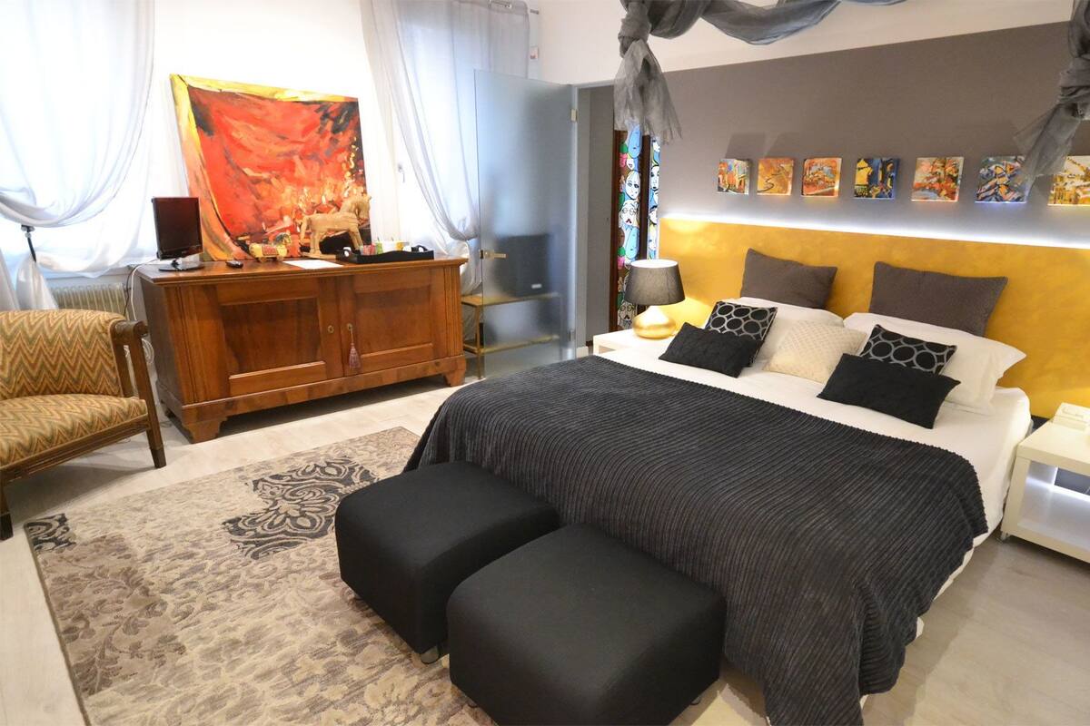 A modern bedroom with a large bed, bedside tables, a dresser, and a painting on the wall.