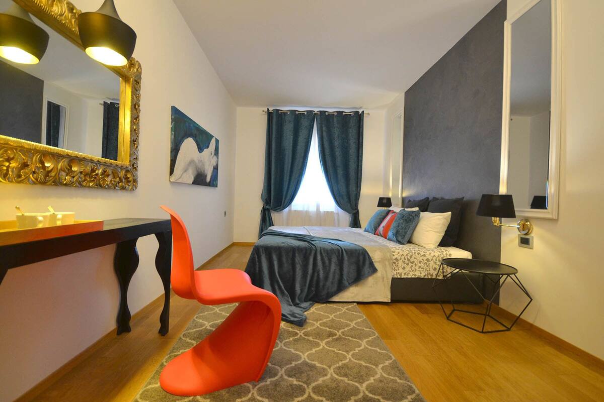 A bedroom with a bed, a desk, a chair, a mirror, and a window with curtains.