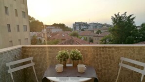 A balcony with a table and two chairs, potted plants, and a view of buildings in the background. - Venice Art Design Bed & Breakfast (Mestre)