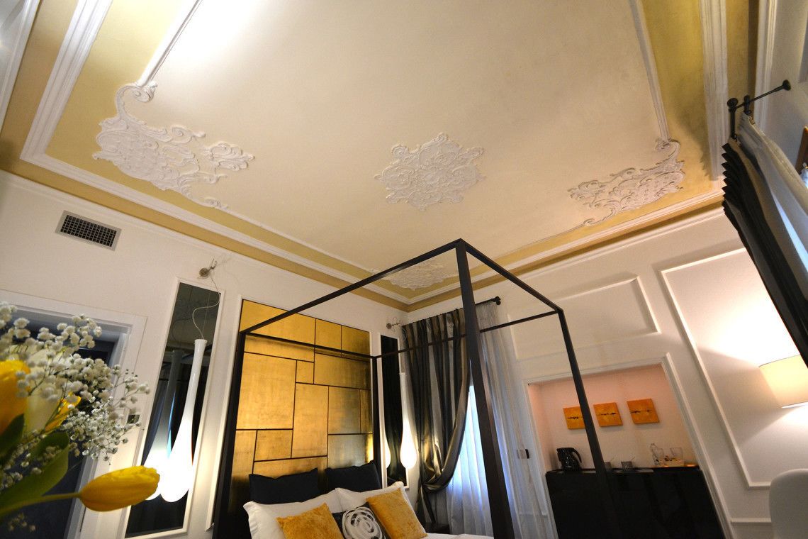 A bedroom with a four-poster bed, a decorative ceiling, and a view of a cityscape.