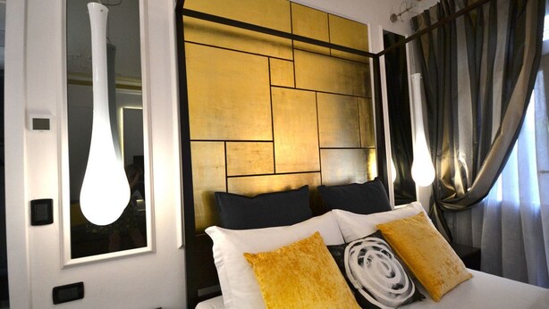 A hotel room with a modern design, featuring a large bed with white and yellow pillows, a headboard with a geometric pattern, and a large window with curtains. - Venice Art Design Bed & Breakfast (Mestre)