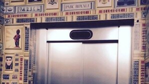 Een lift met een metalen deur, omringd door een muur die versierd is met verschillende ingelijste foto's en tekst, waaronder 