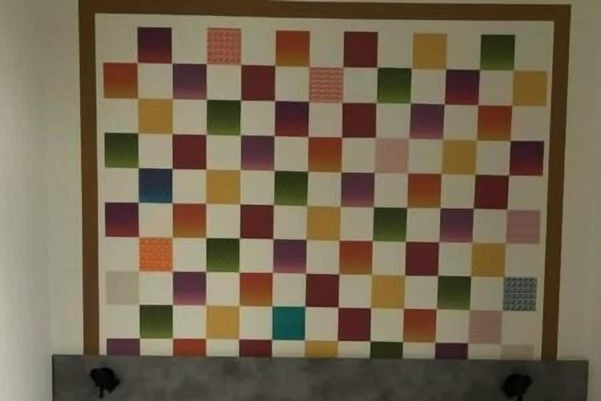 Een hotelkamer met een bed, kussens en een kleurrijk quilt aan de muur.