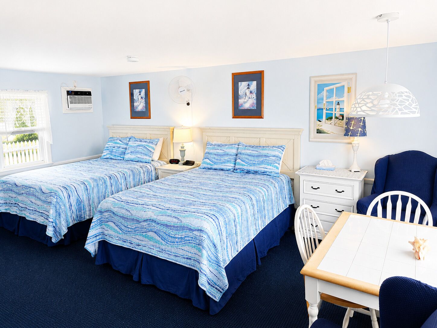 Habitación de hotel con dos camas, un escritorio, una silla y ventana con vista al mar.