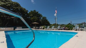 A clear blue swimming pool with a metal ladder, surrounded by lounge chairs and an American flag. - A Beach Breeze Inn (West Harwich)