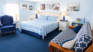 A bedroom with a bed, two bedside tables, a chair, a sofa, and wall art. - A Beach Breeze Inn (West Harwich)