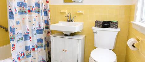 A bathroom with a shower curtain, sink, toilet, and a framed sign on the wall.