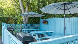 A blue outdoor seating area with picnic tables and umbrellas, surrounded by a wooden fence and trees. - A Beach Breeze Inn (West Harwich)
