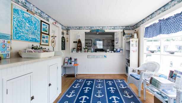 A room with nautical-themed decor, including a map, anchor-patterned rug, and a view of the sea through the window. - A Beach Breeze Inn (West Harwich)