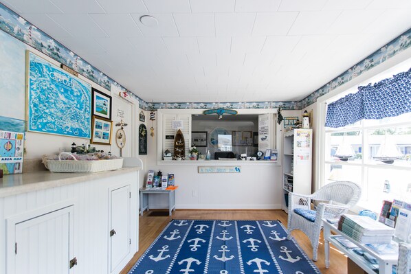 A room with nautical-themed decor, including a map, anchor-patterned rug, and a view of the sea through the window.