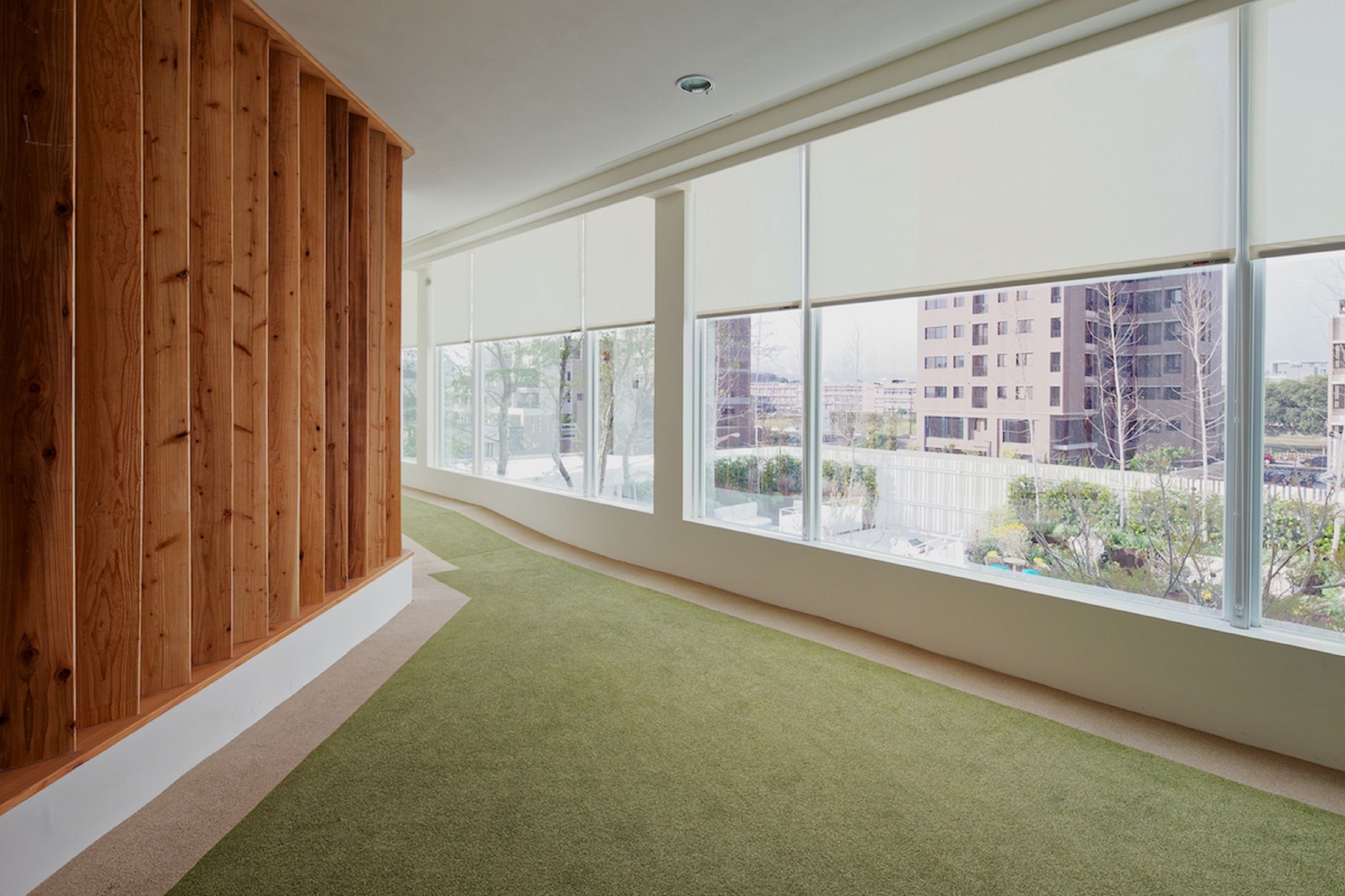 A spacious room with large windows, a wooden panel wall, and a green carpet.