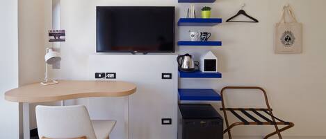 Una habitación moderna con televisor de pantalla plana, un escritorio con silla, un altavoz negro pequeño, un sillón colgante y estantes con objetos decorativos.