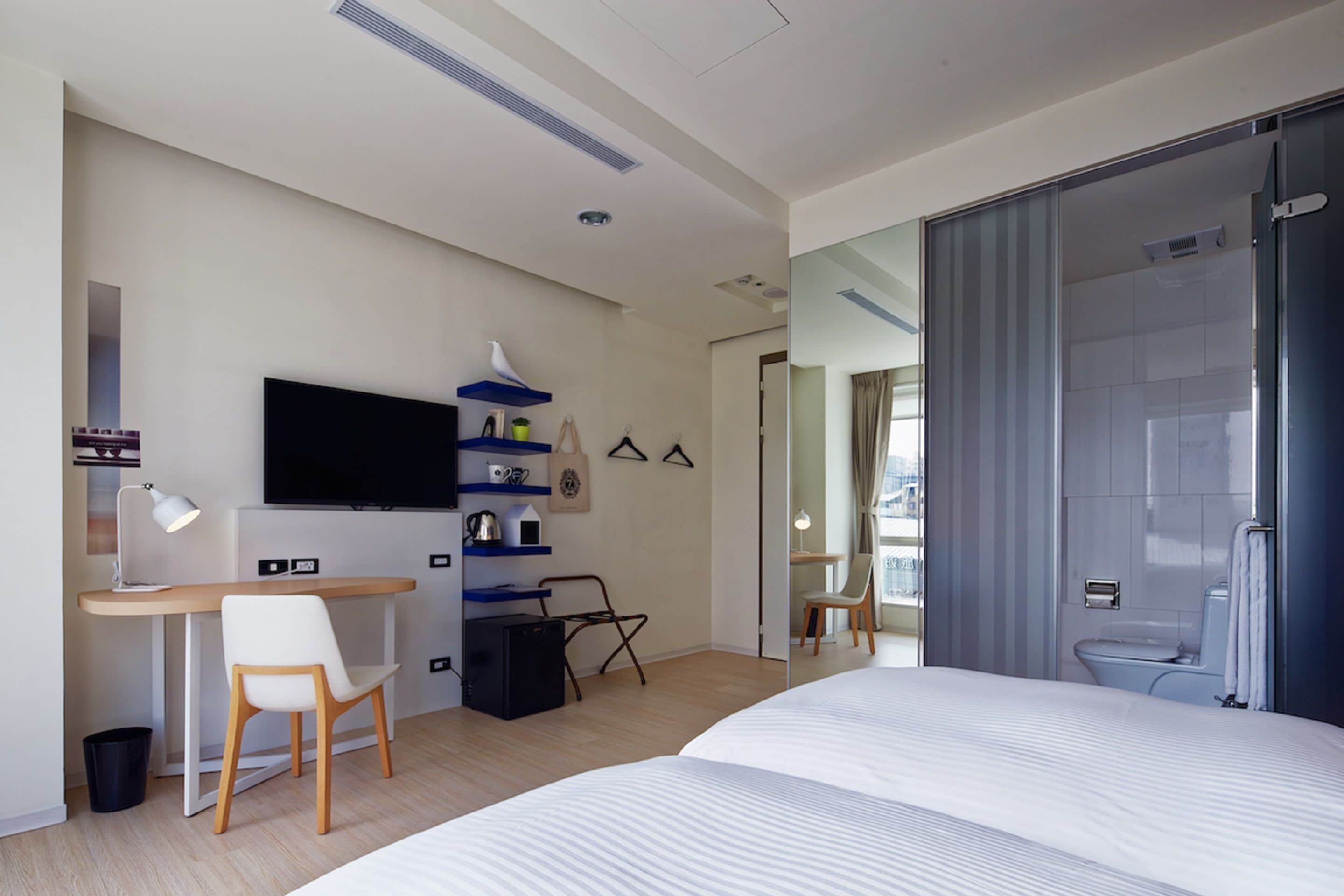 Une chambre d’hôtel moderne équipée d’un lit, d’un bureau, d’une chaise, d’une télévision et d’un espace douche.