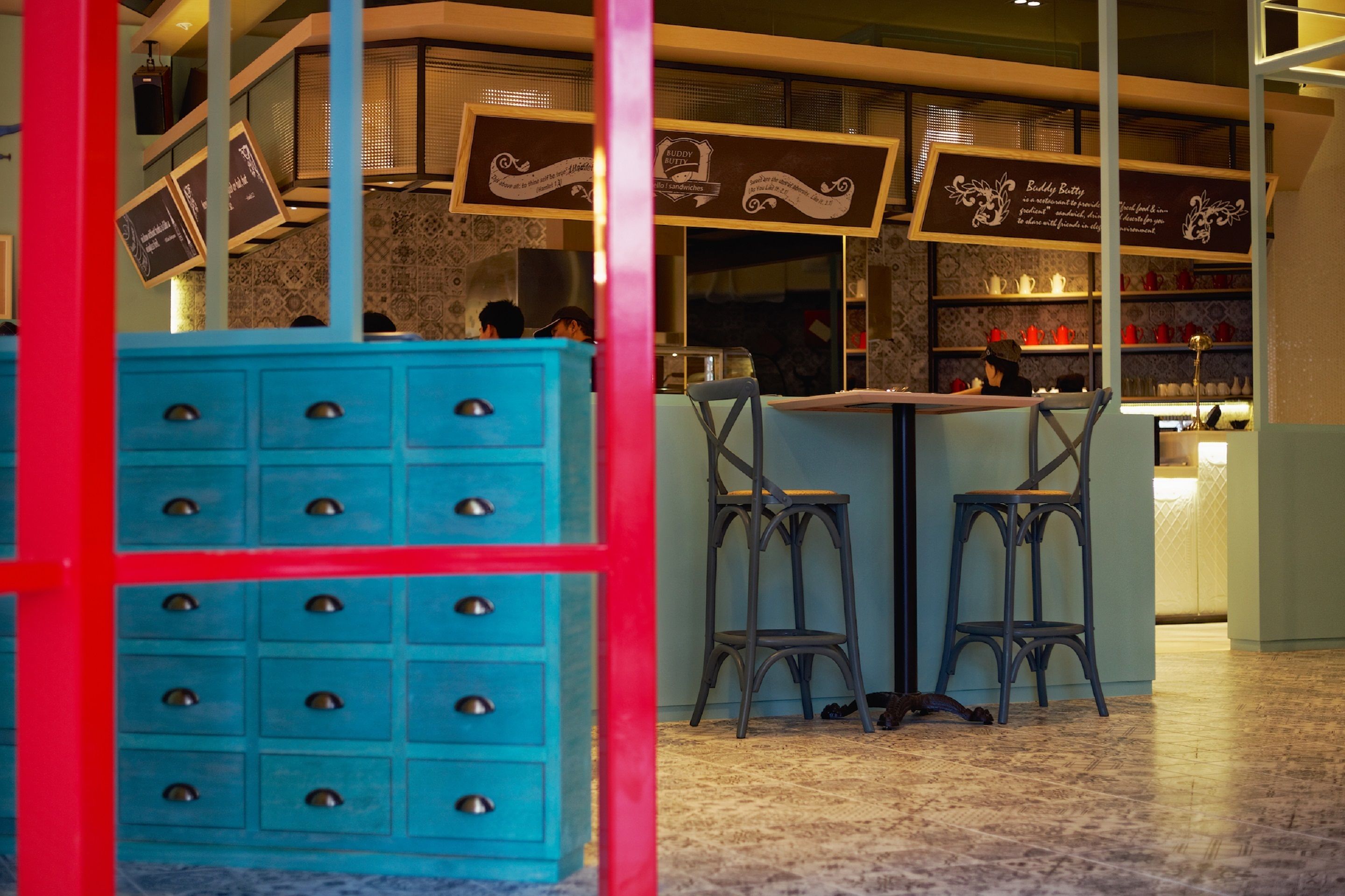A restaurant interior with a blue counter, bar stools, and hanging menu signs.