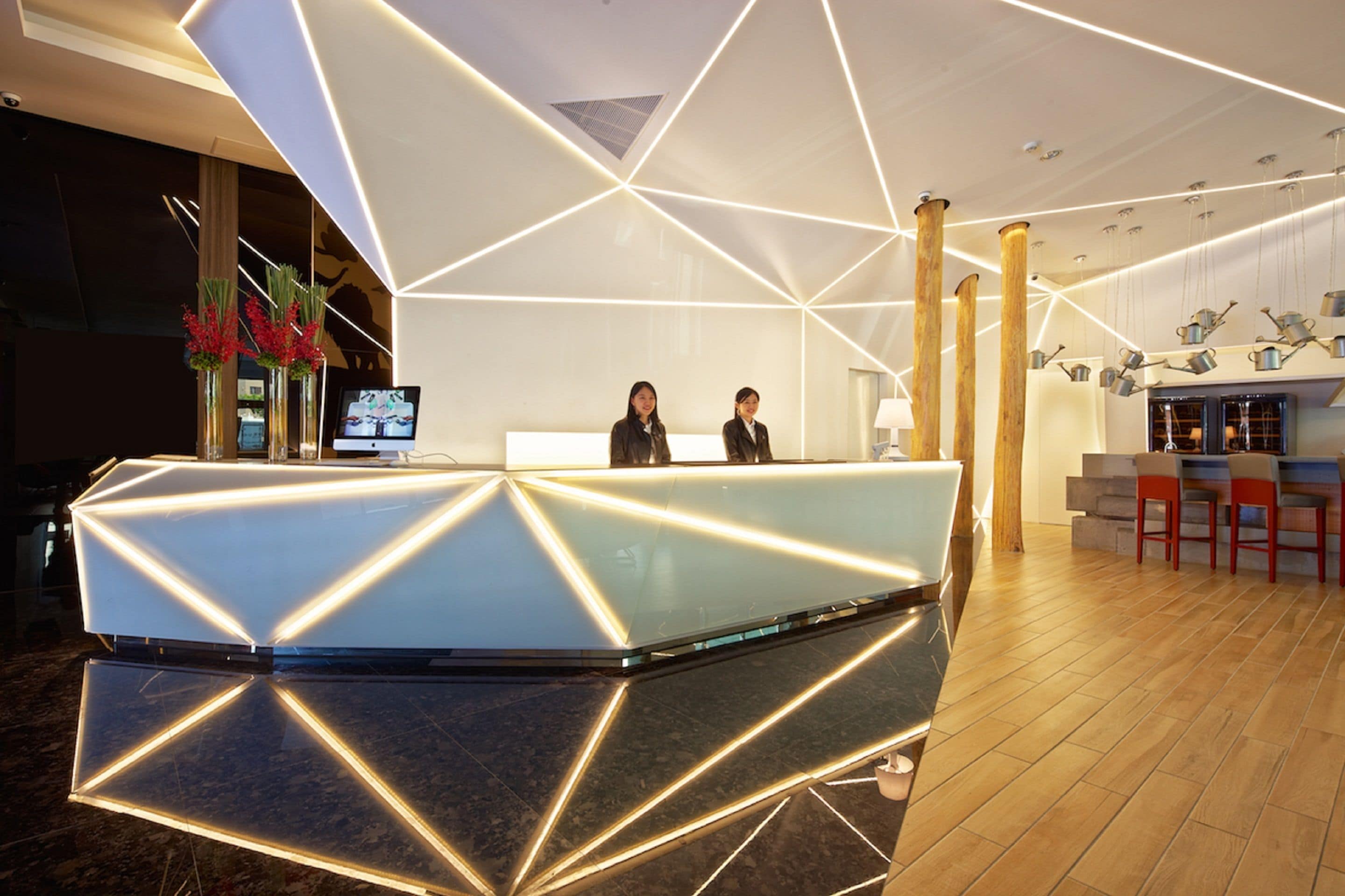A modern reception area with a geometric light design, a reception desk, and a bar area with stools.