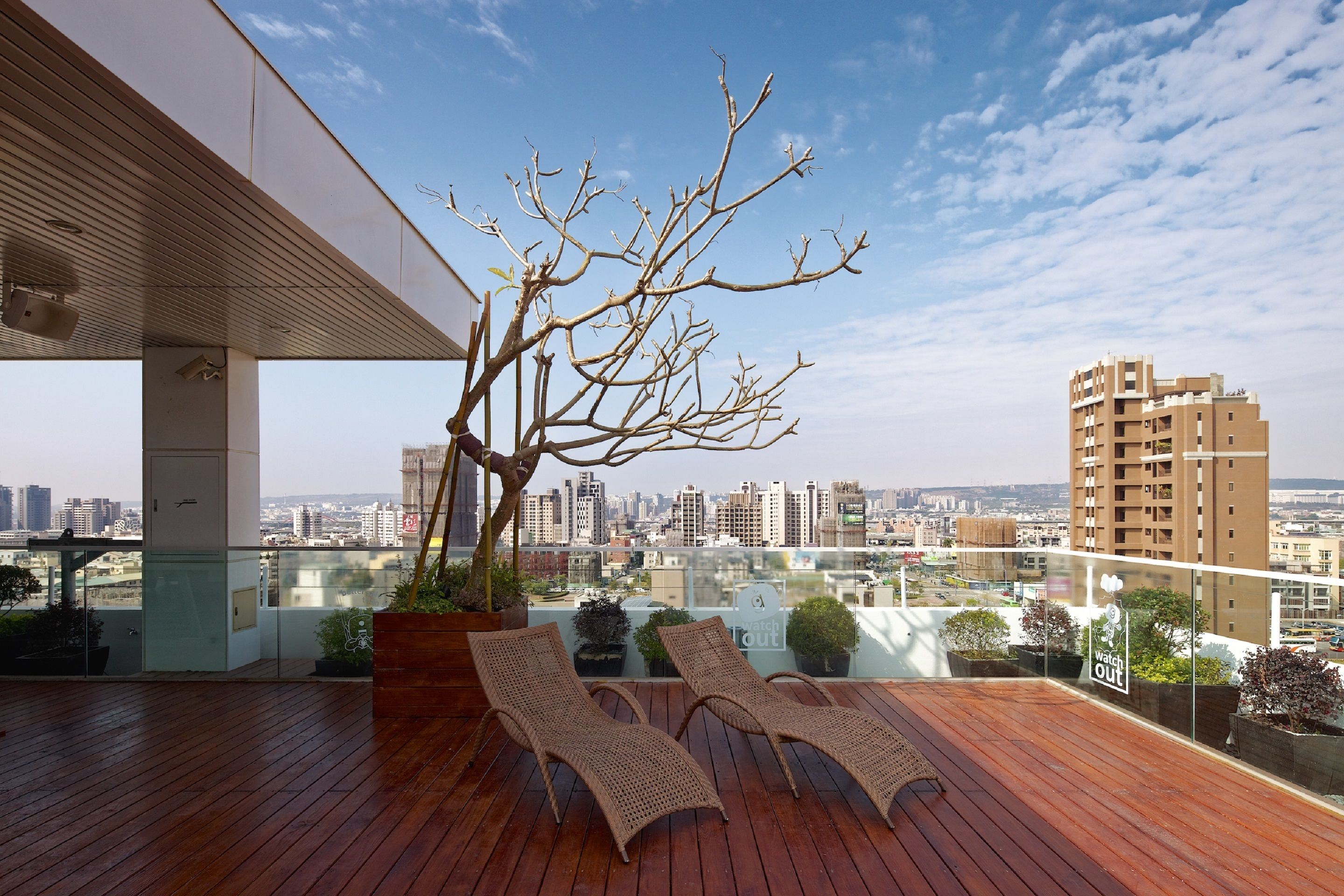 A rooftop terrace with two lounge chairs, a tree, and a city view.