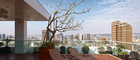 A rooftop terrace with two lounge chairs, a tree, and a city view.