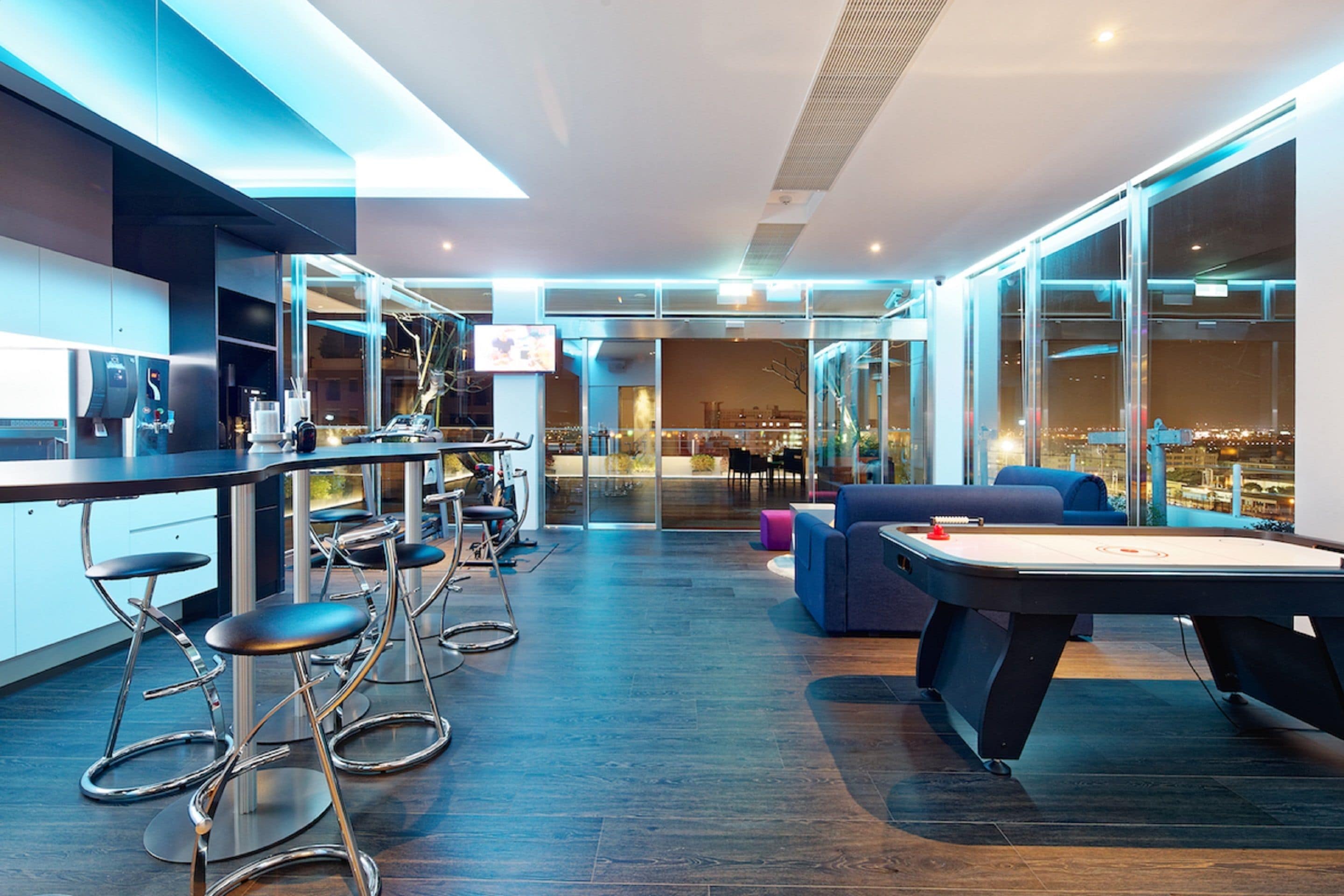 A modern lounge area with a pool table, bar stools, and a sofa.