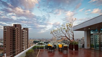 A rooftop terrace with a wooden deck, outdoor seating, and a view of the cityscape.