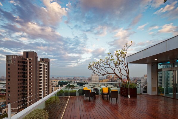 Una terraza en la azotea con piso de madera, mobiliario exterior y vista panorámica de la ciudad.