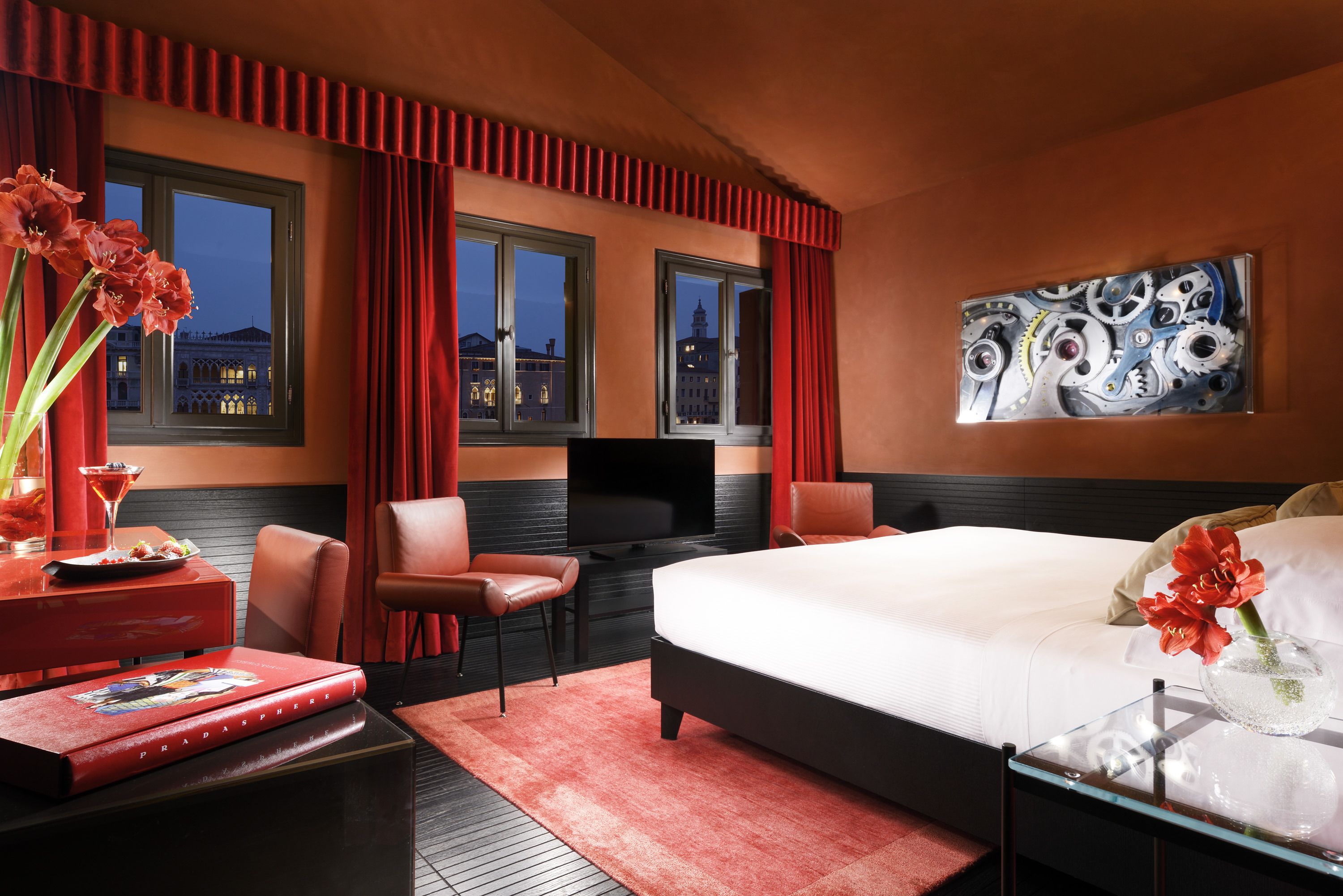 Quarto de hotel moderno com uma cama grande, TV e vista para a paisagem urbana pelas janelas.