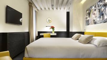 Una habitación de hotel moderna con una cama grande, un televisor de pantalla plana, una mesita con un jarrón de flores y una pieza de arte único en la pared.