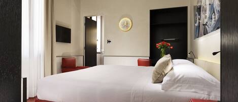 A hotel room with a large bed, a red chair, a small table, a wall-mounted TV, and a painting.