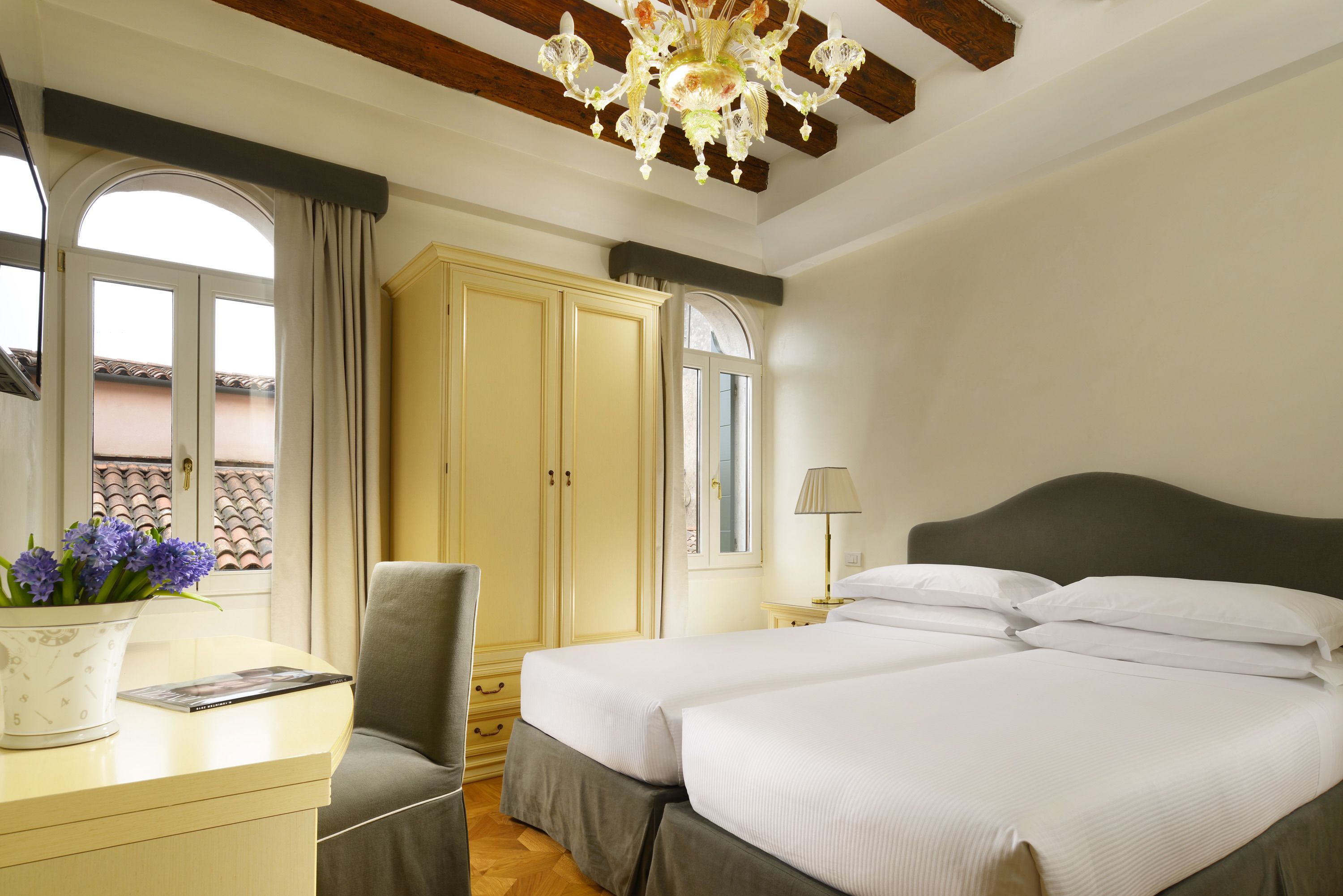 Una habitación de hotel con cama, escritorio, silla, armario y ventana con cortinas.