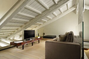 Um quarto moderno no estilo loft com teto inclinado, uma janela grande, uma televisão de tela plana, uma mesa de centro de madeira e um sofá.