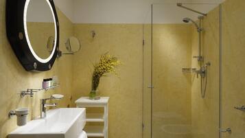 A bathroom with a large mirror, a white sink, a glass shower enclosure, and a vase with yellow flowers on a small shelf.