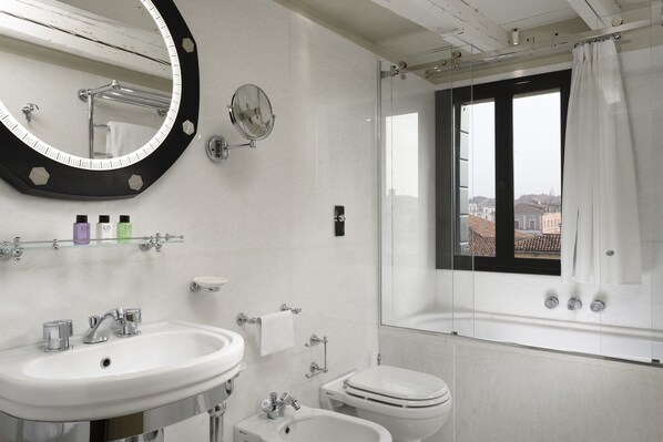 Un bany modern amb un mirall gran, un lavabo, una tassa i un vàter. Hi ha una finestra amb vistes a edificis a l'exterior.