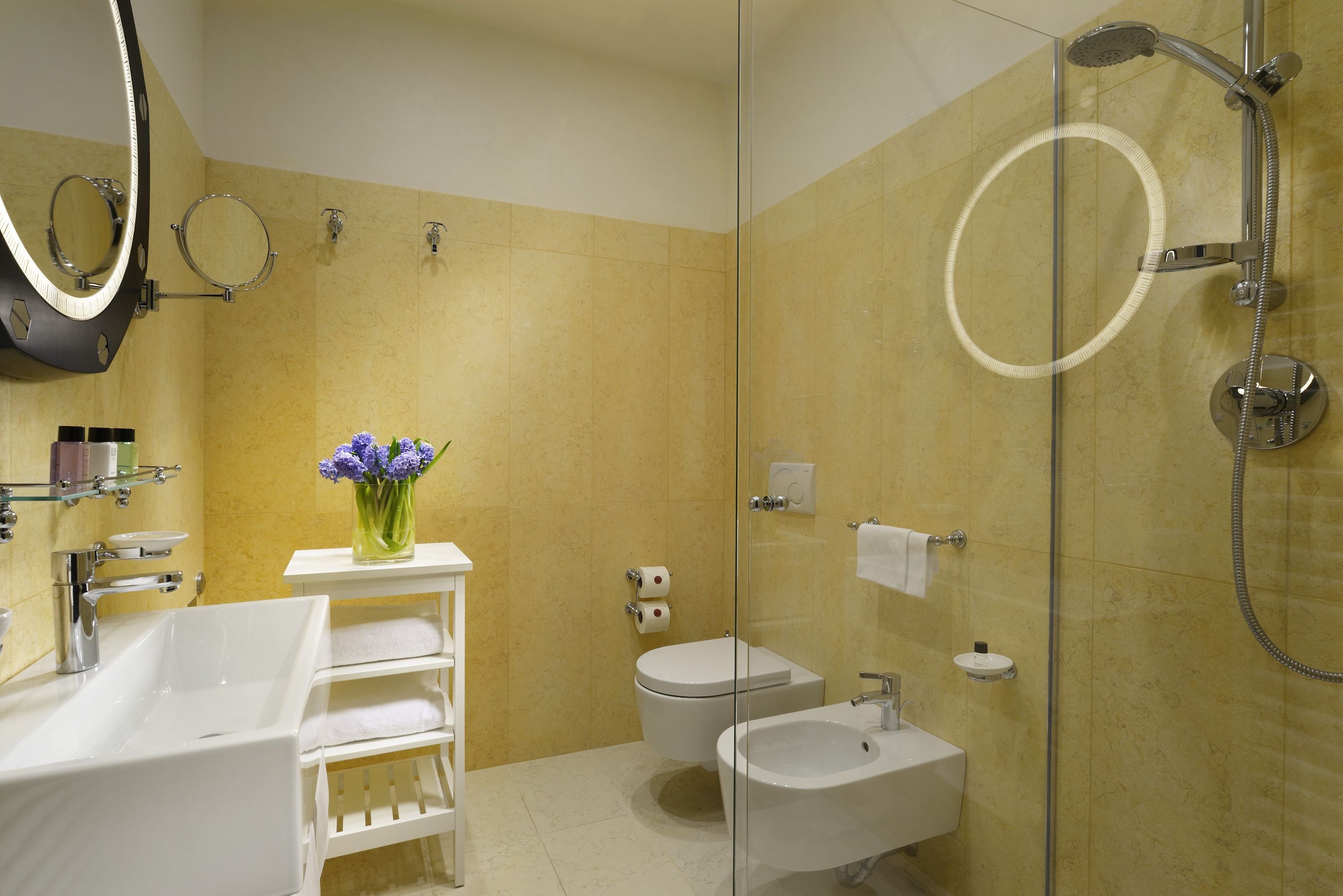 A modern bathroom with a large sink, a bidet, a glass-enclosed shower, and a mirror with a light.