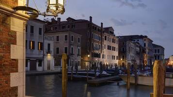 A canal with buildings on either side, wooden posts in the water, and a street lamp on the left.