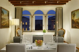 Comedor con una mesa dispuesta para cuatro, un jarrón de flores y vistas de edificios a través de una ventana.