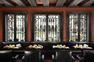 Escena de desayuno con mesas, sillas y una vista a través de ventanas decorativas.