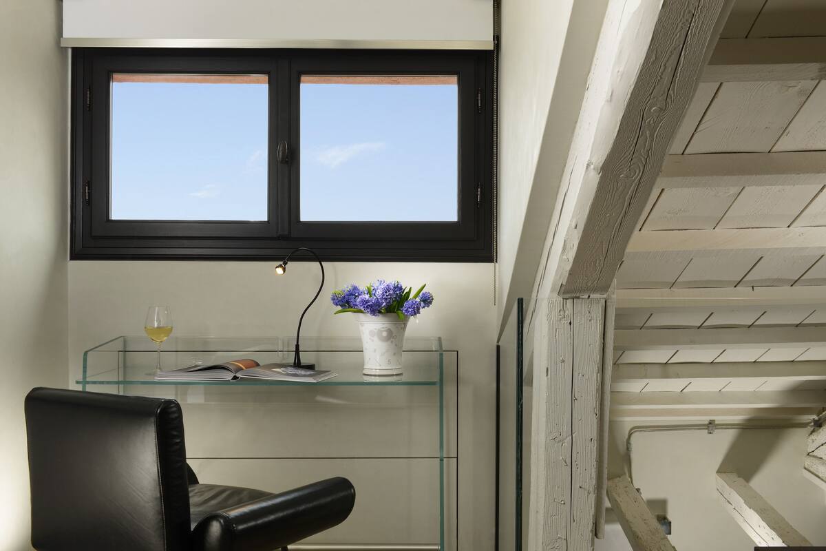 A modern room with a glass desk, a black leather chair, a window with a view, and a staircase.