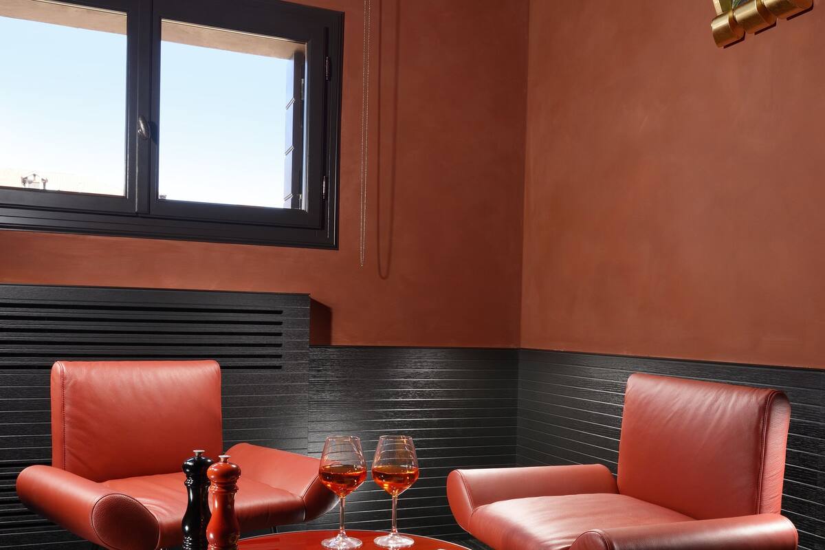 A modern room with two red leather chairs, a small round table with a red base, two wine glasses, and a pepper grinder.