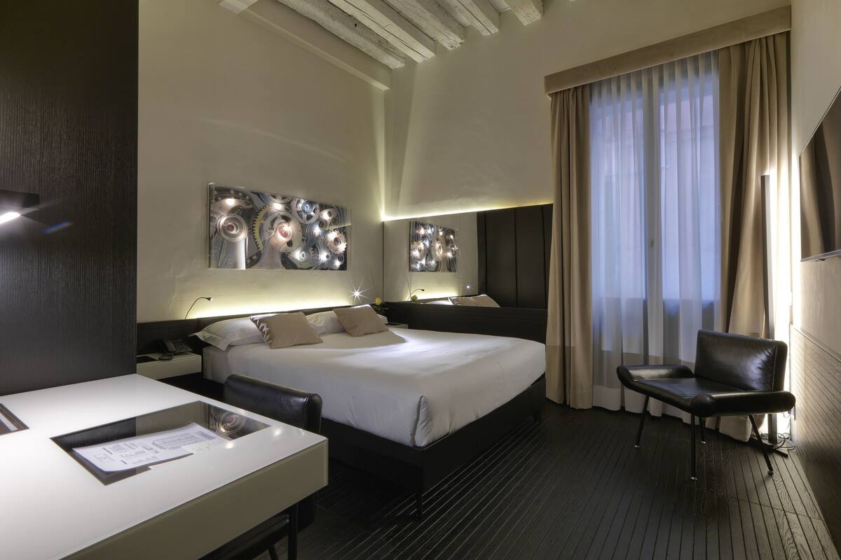 A modern hotel room with a large bed, a desk with a chair, and a seating area.