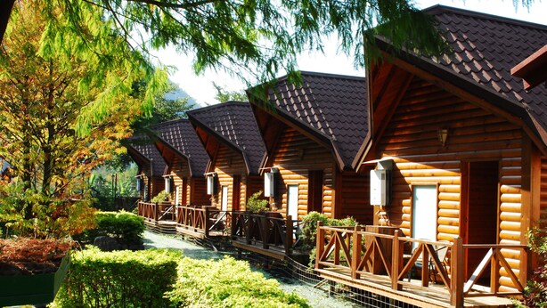 A row of log cabins with wooden decks and railings, surrounded by greenery and a small pond. - Tai Yi Red Maple Resort (Puli)