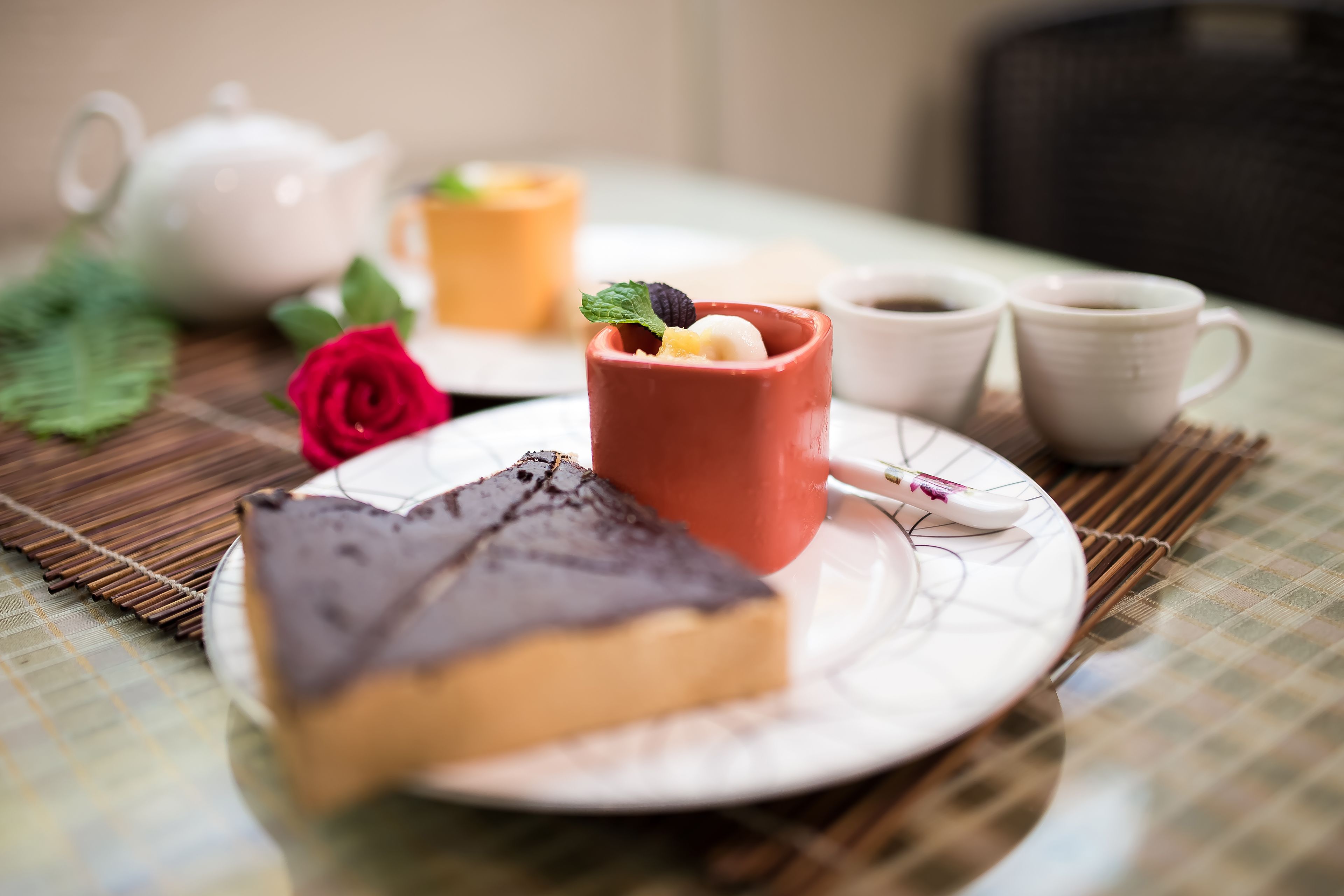A dessert plate with a slice of cake, a small cup with a dessert, and two cups of coffee on a table with a placemat.