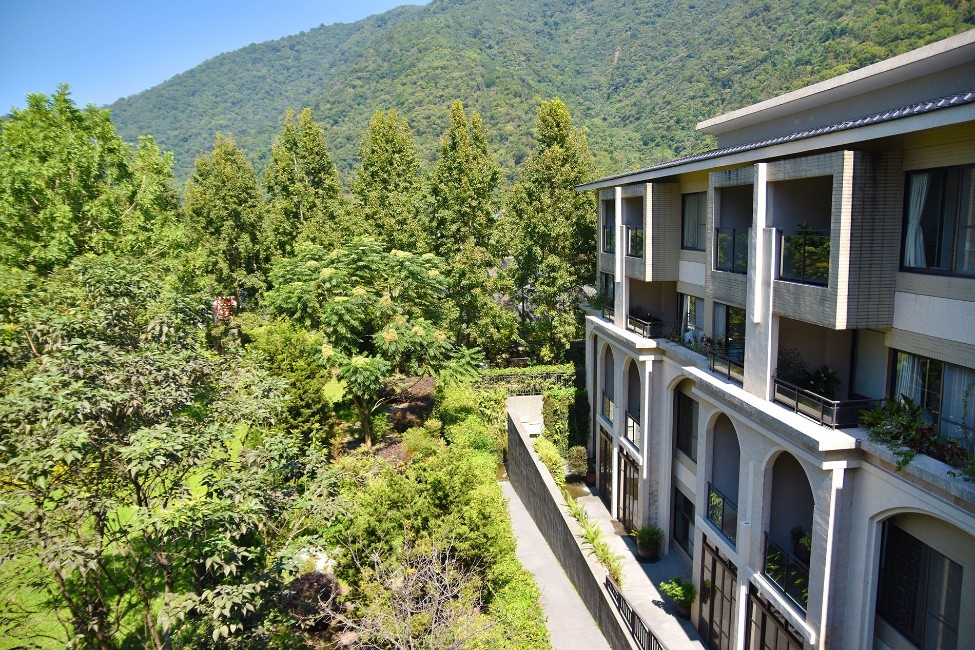 A multi-story hotel with balconies, surrounded by dense greenery and a mountainous backdrop.