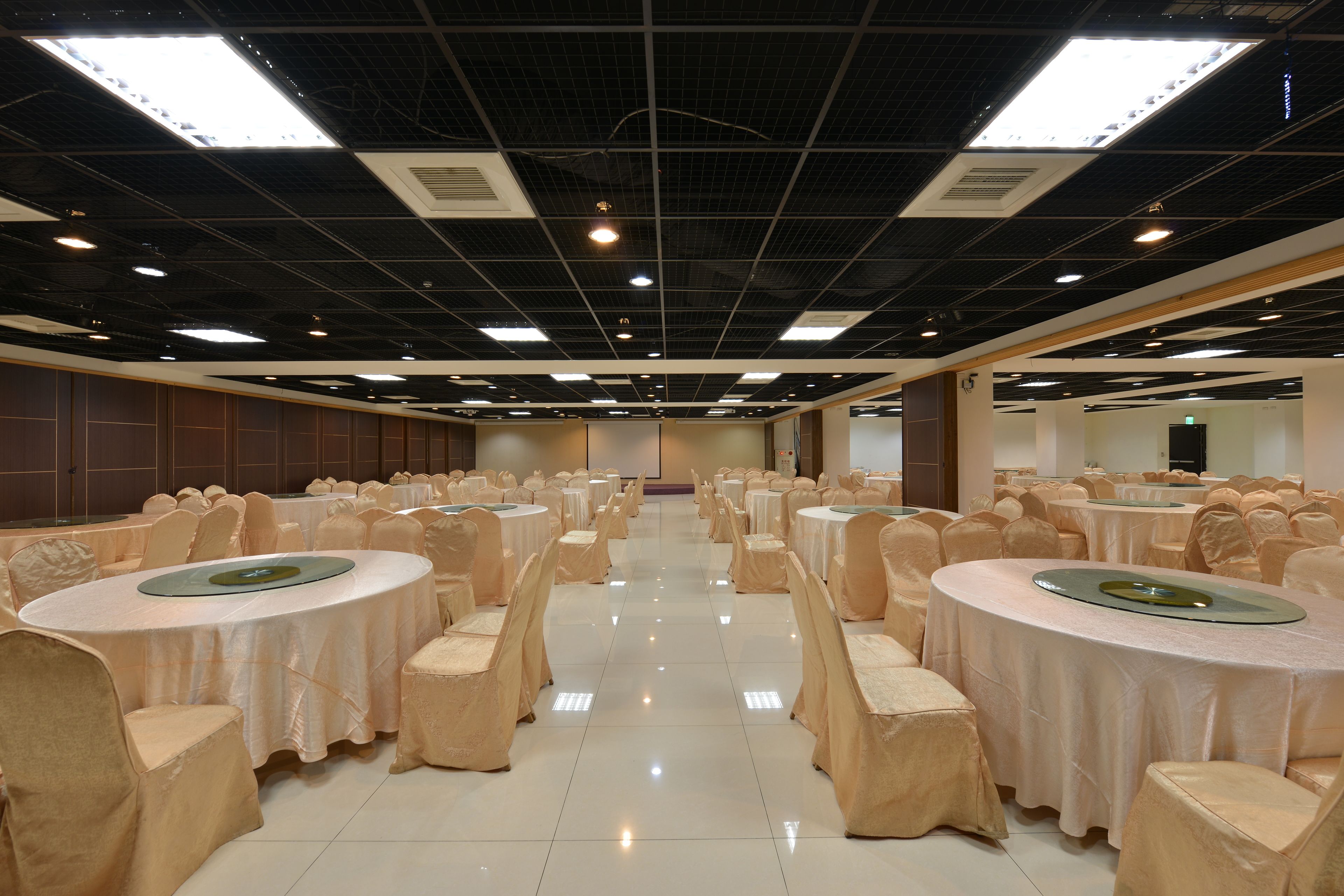 A banquet hall with round tables, chairs, and a high ceiling with lighting fixtures.