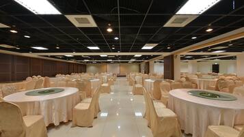 A banquet hall with round tables, chairs, and a high ceiling with lighting fixtures.